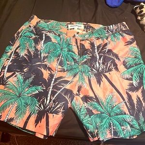 A pair of swimming trunks light pink as the base color, with palm trees